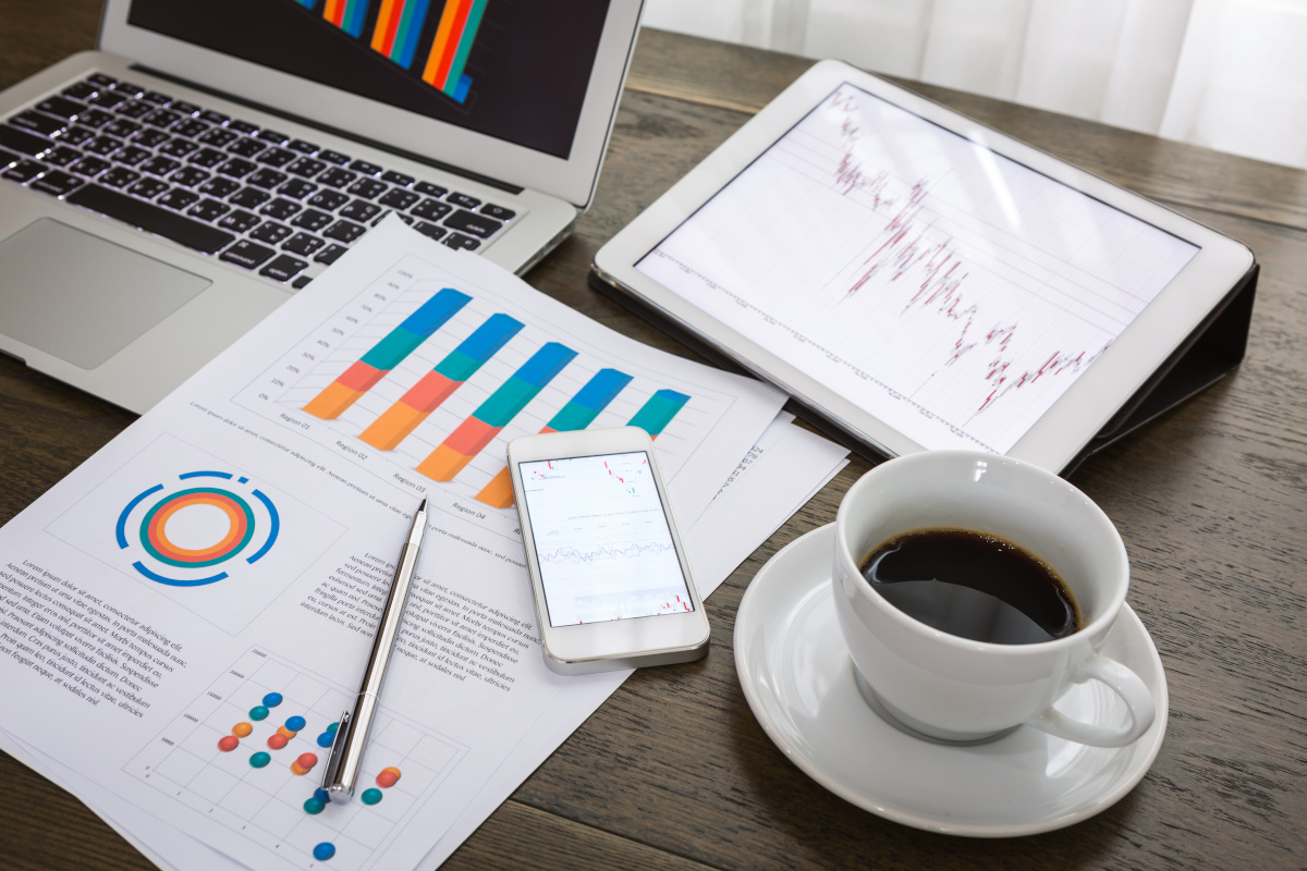 Various reports on a desk next to a coffee cup and a laptop