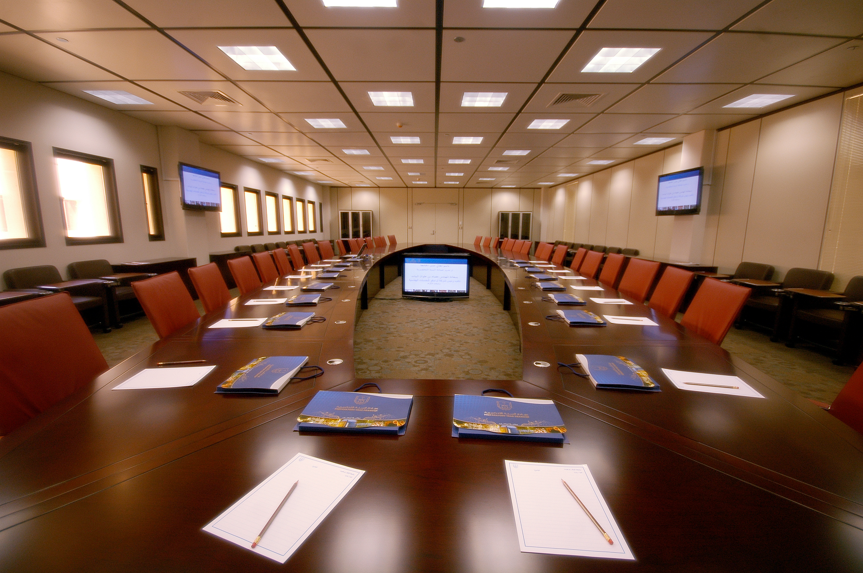 Large empty conference room with center computer, paper and pad at each seat