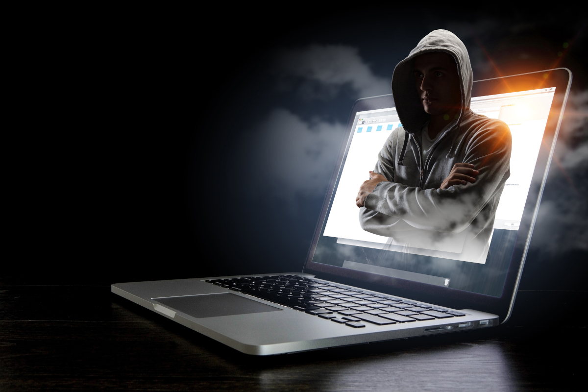 A hacker with his arms crossed coming out a laptop screen
