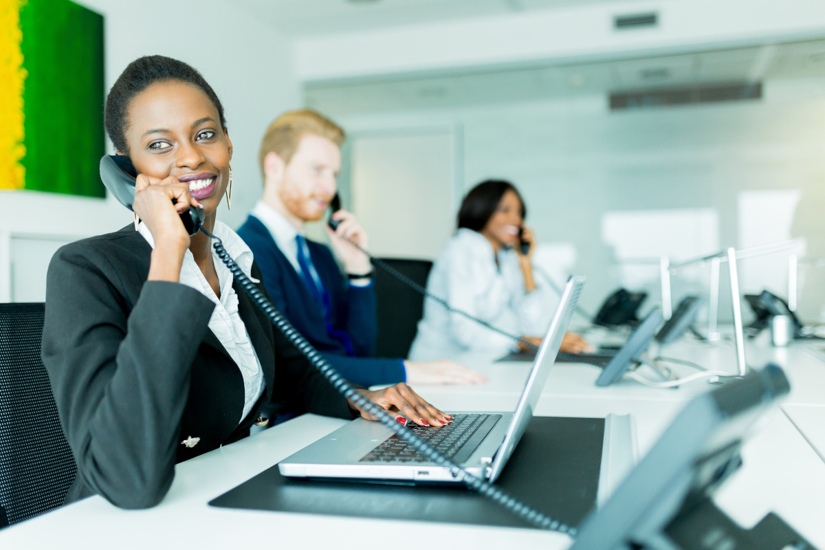 Smiling service representatives seated in a row at long desk answering phones.