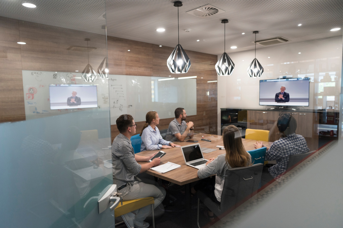 Business team in meeting room using multiple mobile devices while on video conference call.