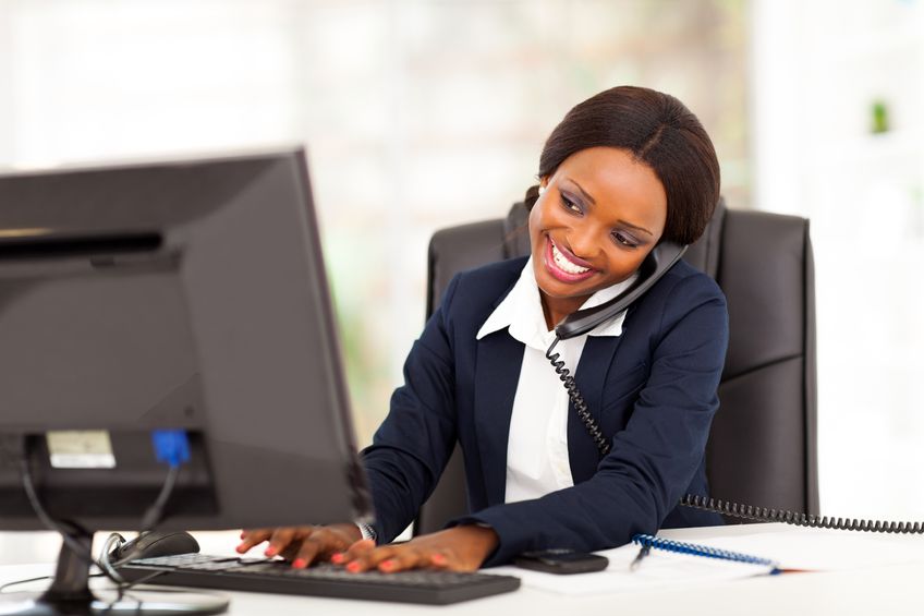 Smiling businesswoman in blue jacket talking on phone at her work desk