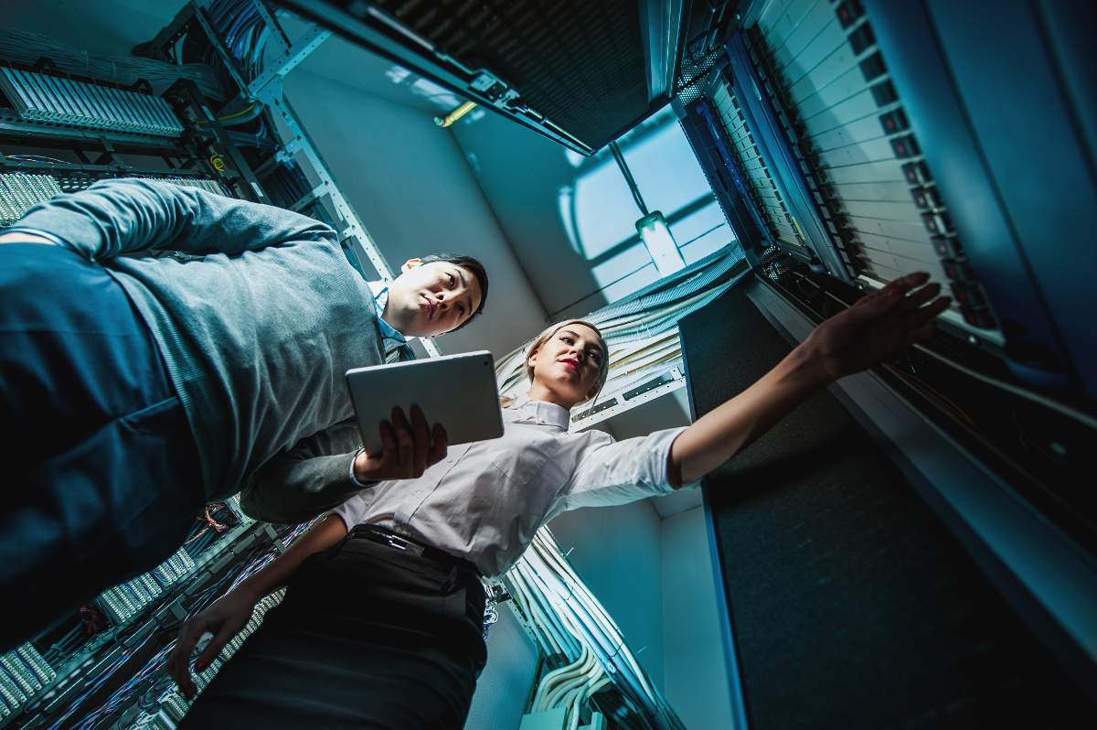 Two technicians looking at a tablet while working on the cabling at a network rack