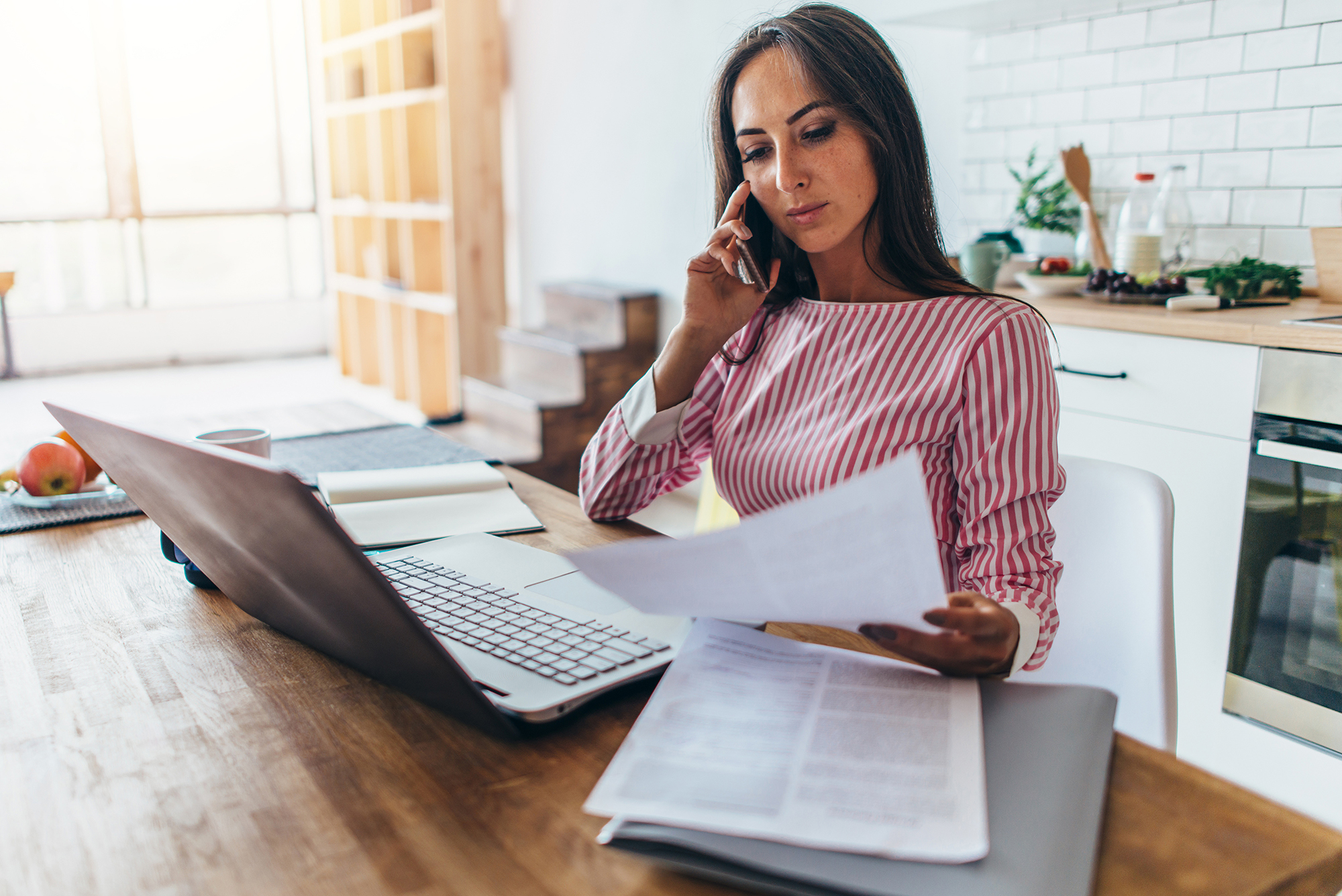 A women working from home, reviewing documents while on the phone