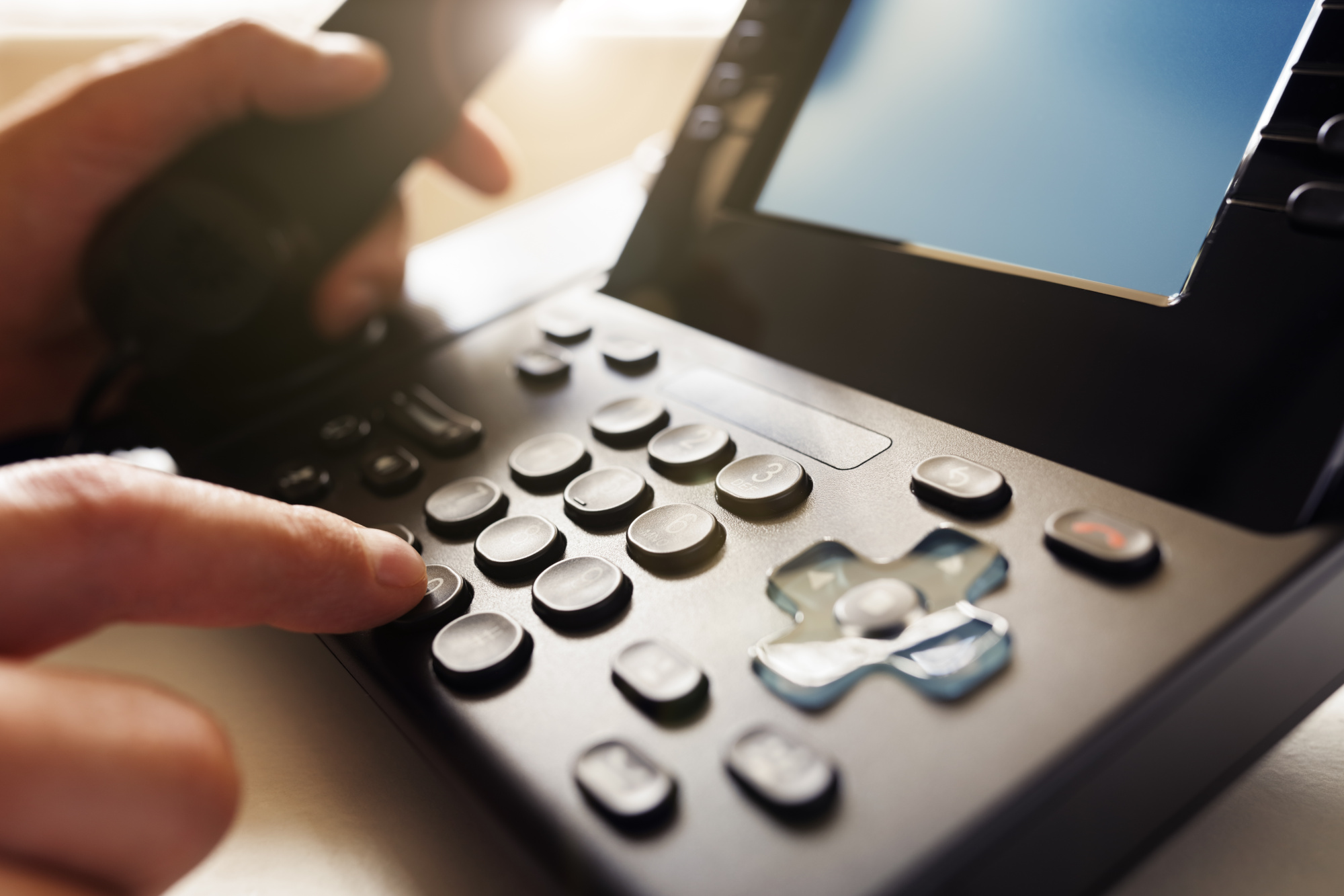 Close up of a person using the dail-pad of a office phone base