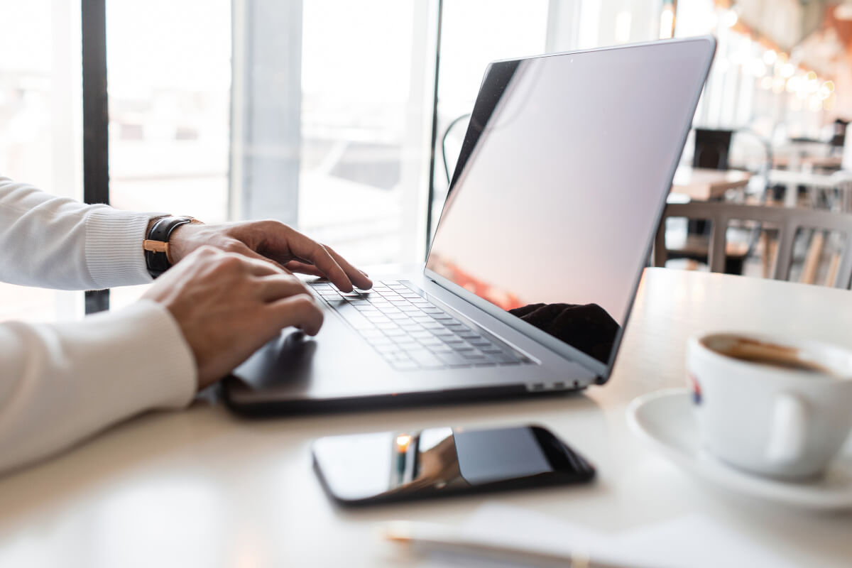 Male using laptop with mobile phone sitting on table next to it